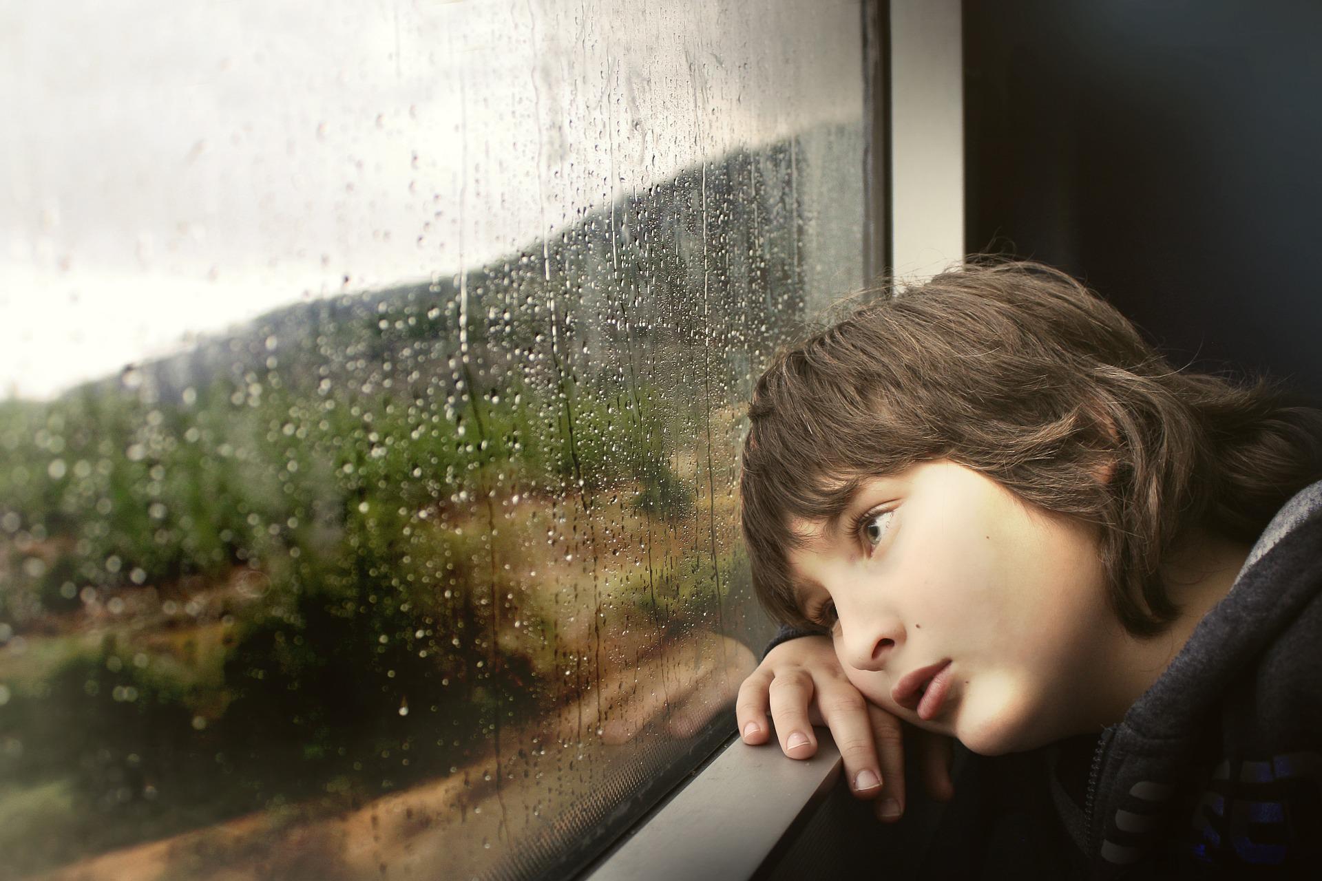 Boy looking sadly out of a window. 