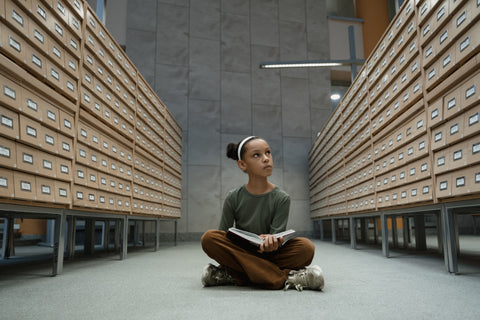 Child sitting among a card filing system, reading a book
